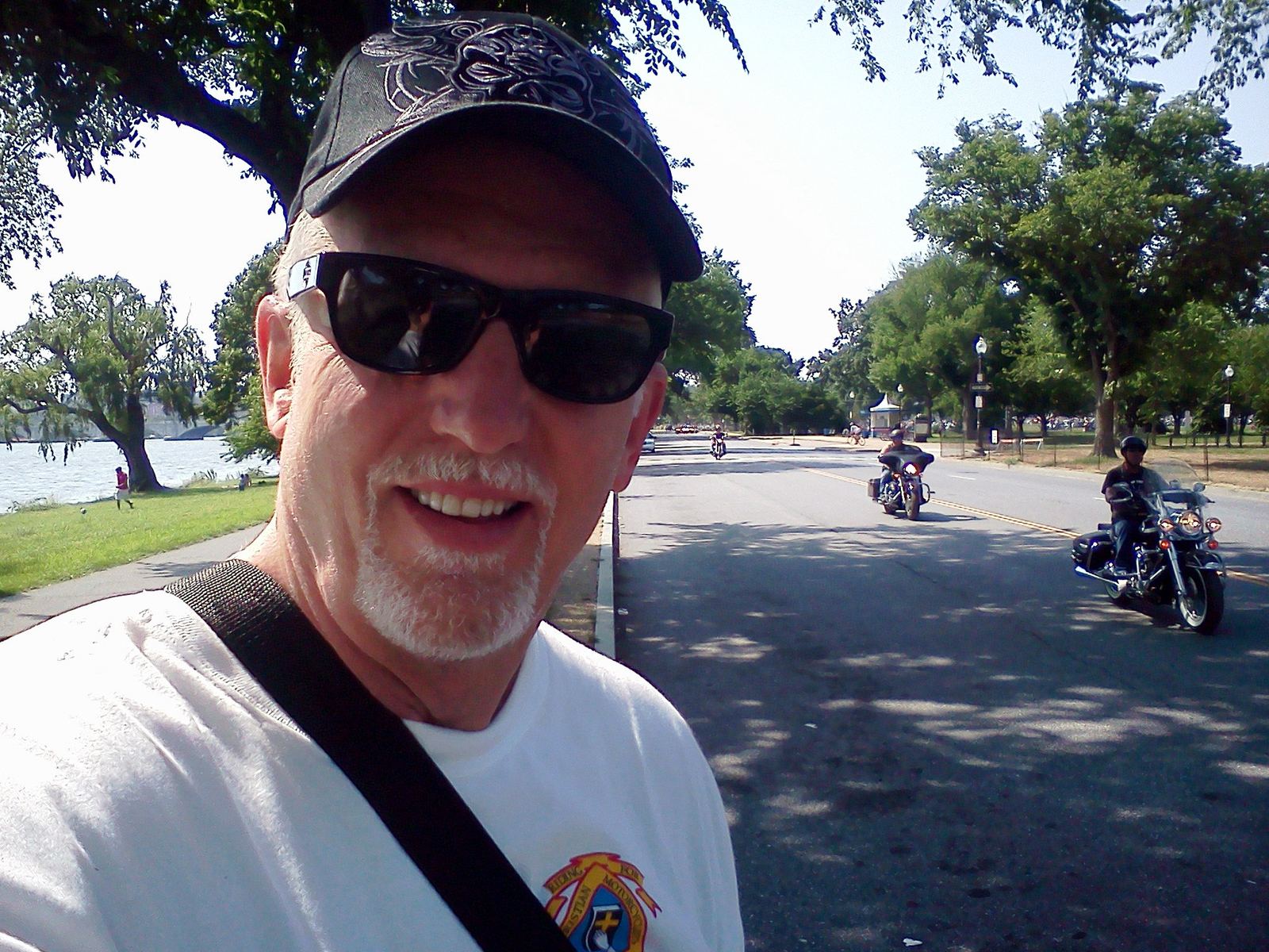 Tom Hughes with riders passing by on a tree-lined road along the Potomac at Rolling Thunder