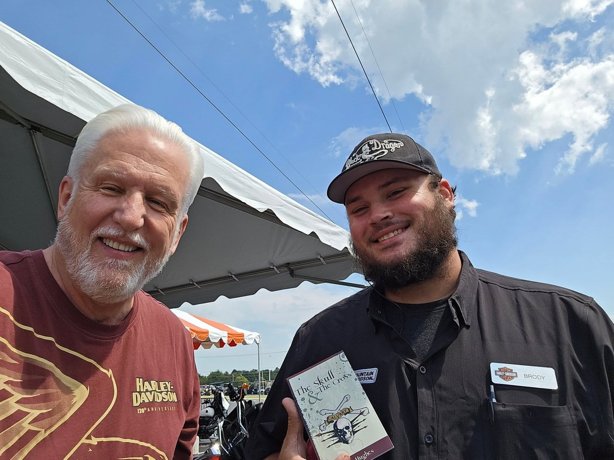 Tom Hughes giving a copy of The Skull & The Cross to a Harley-Davidson dealership employee