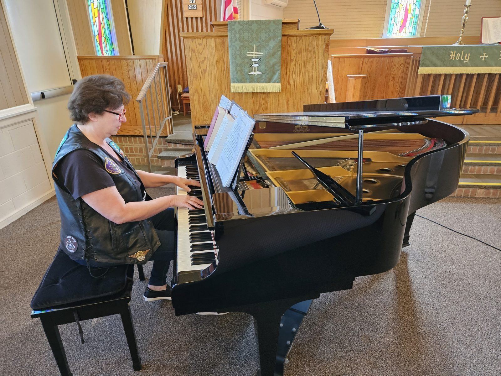 Cathy Hughes in her patched leather vest playing a grand piano at the front of a church