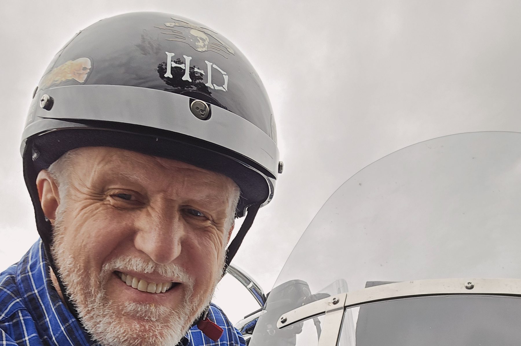 Tom Hughes smiling in his H-D helmet beside his Harley's headlight