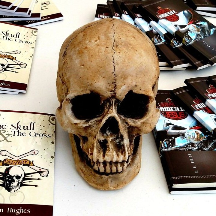 Copies of The Skull & The Cross and The Ride of Your Life fanned out on a table around a real skull