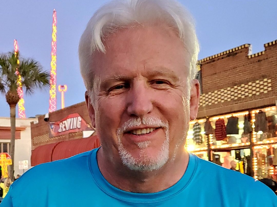 Tom Hughes in an Adventist Motorcycle Ministry shirt on a boardwalk at sunset