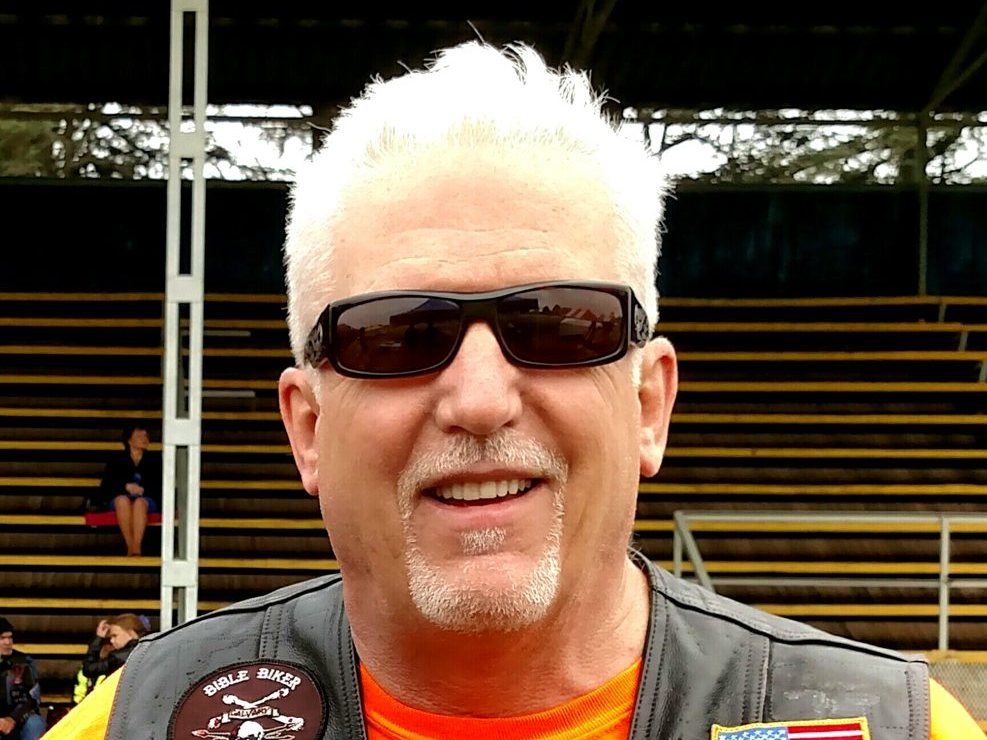 Tom Hughes in his patched vest and sunglasses at a rally grandstand