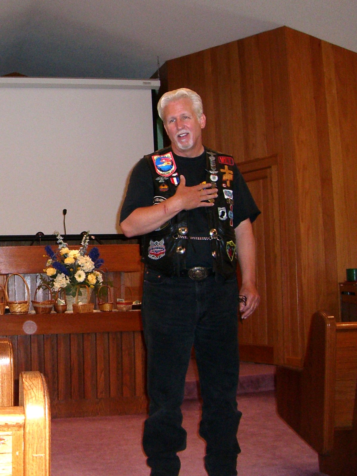 Pastor Tom Hughes preaching in his patched leather vest, up front in a church